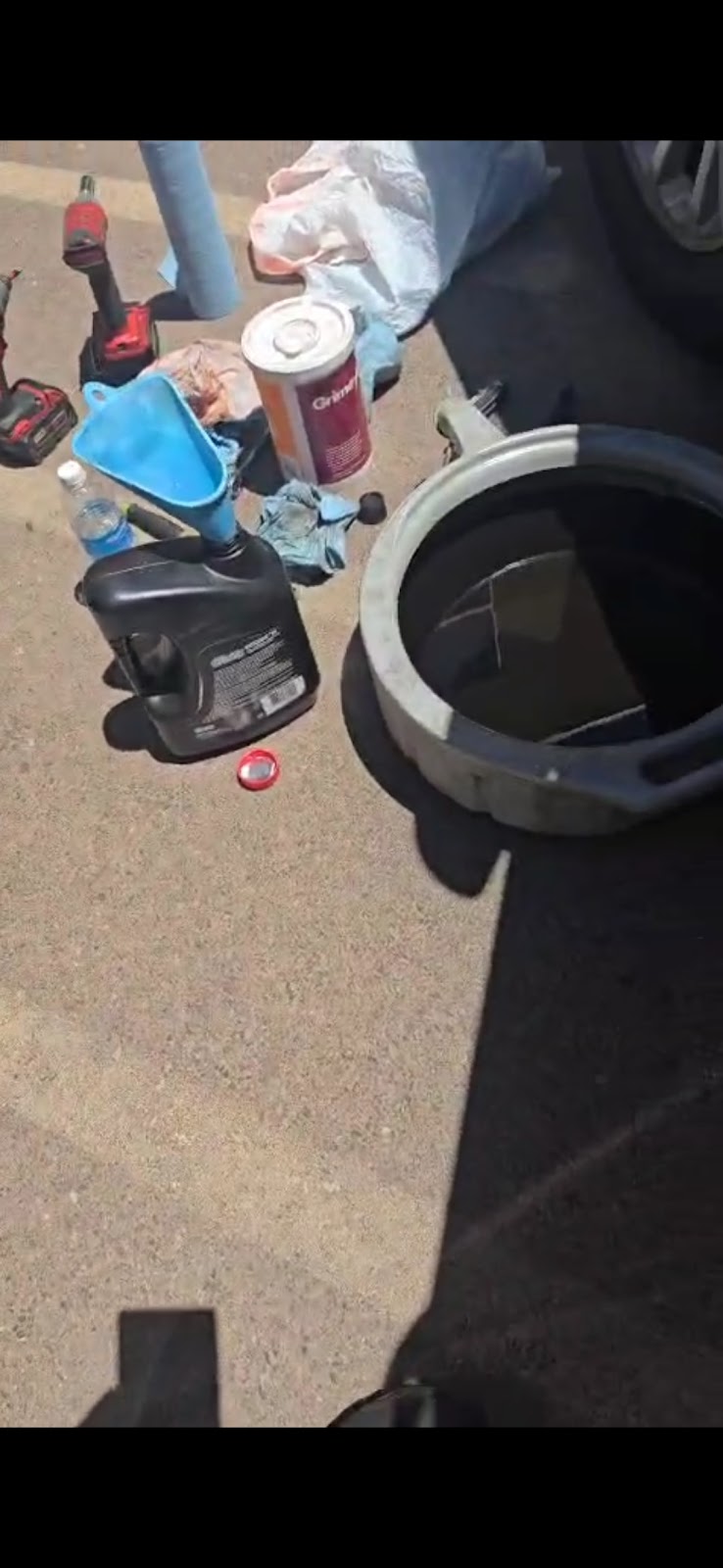 Fluid service laid out on the asphalt: drain pan, funnel, fresh fluid, and impact tools